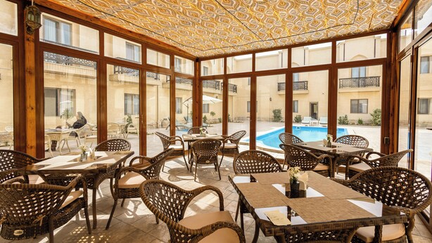 Ein Außenbereich zum Essen mit Korbmöbeln und einer gemusterten Decke, mit Blick auf einen Pool und Gebäude.