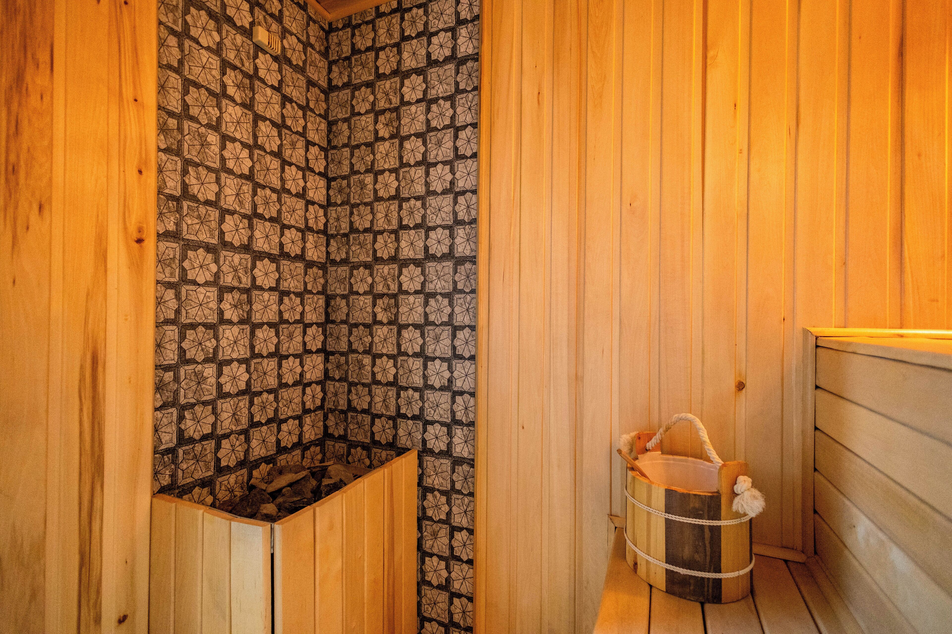 A wooden sauna with a patterned tile wall, a wooden bench, and a bucket with a towel.
