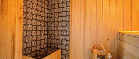 A wooden sauna with a patterned tile wall, a wooden bench, and a bucket with a towel.