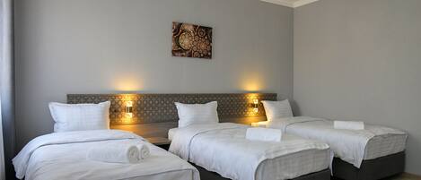A hotel room with three beds, a decorative wall piece, and two wall-mounted lights.