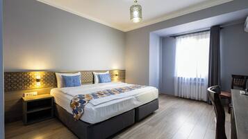 A hotel room with a large bed, bedside tables, a desk, and a window with curtains.