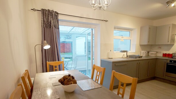 Een moderne keuken met een eethoek, met een tafel en stoelen, een kroonluchter en uitzicht door een glazen deur.