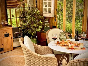 A wicker dining table with a wine glass, a bottle of wine, and a cheese board. - Le Chat Vert - Gîte de Charme**** (Saint André)