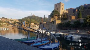 Un port històric amb vaixells amarrats, una torre de pedra i un turó amb edificis al fons.