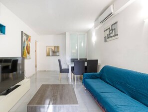 A modern living room with a flat-screen TV, a blue sofa, a dining area with a table and chairs, and a kitchen area with a refrigerator. - Centre APT in St Julians/PV with spacious living (San Ġiljan)