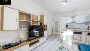 A modern kitchen with white cabinets, a large black TV, and a glass dining table. - Spacious, central APT in Paceville/St Julians. (San Giljan)