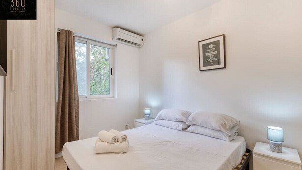 A bedroom with a bed, a nightstand, a bedside lamp, a window with curtains, an air conditioning unit, and a framed quote on the wall. - Spacious, central APT in Paceville/St Julians. (San Giljan)