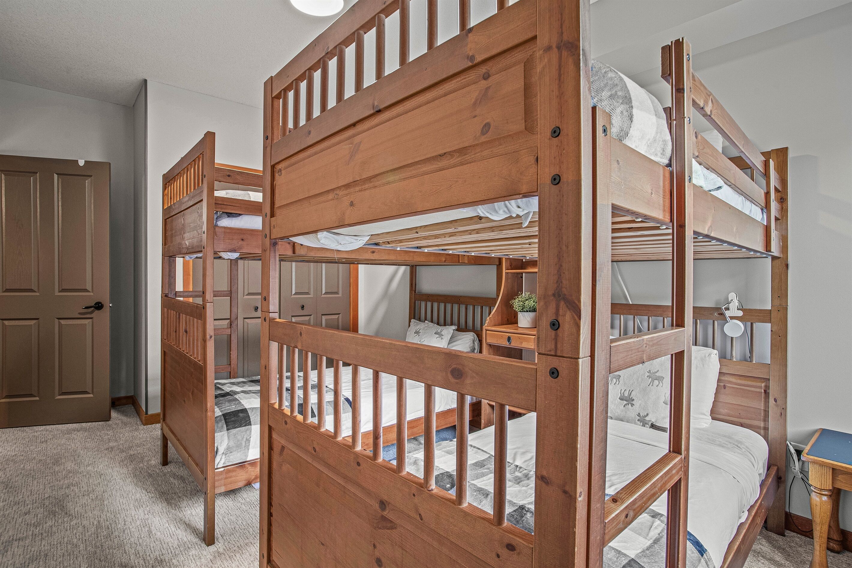 A bunk bed room with a wooden headboard, a bedside table with a lamp, and a door.