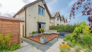 Een huis met een houten terras, een kleine tuin en een tuinhuis.