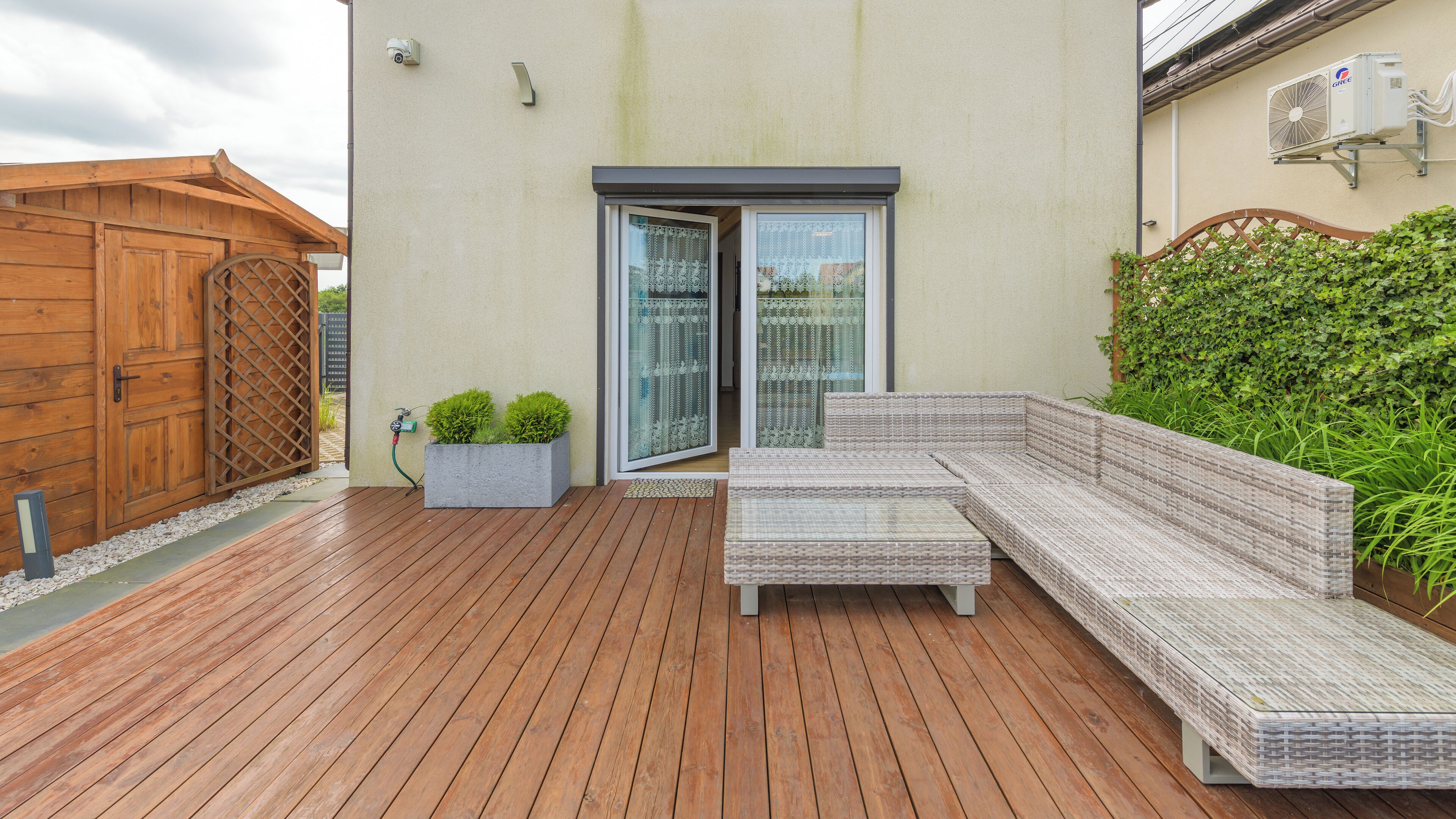 A wooden deck with a wicker sofa and a planter with small plants.