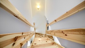 Een houten trap met een leuning, leidend naar een kamer met een wit plafond en een lamp.