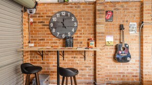 A brick wall with a large clock, a guitar, and a table with stools.