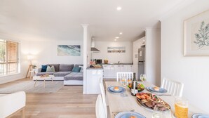 A modern living space with a dining area, kitchen, and a sofa set. - Pet friendly Driftwood Cottage, 1-28 Farm Rd - W-Fi, Air Con and ground floor (Fingal Bay)