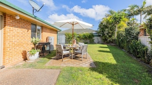 A backyard with a patio table and chairs, a satellite dish, and a brick house. - Pet friendly Driftwood Cottage, 1-28 Farm Rd - W-Fi, Air Con and ground floor (Fingal Bay)