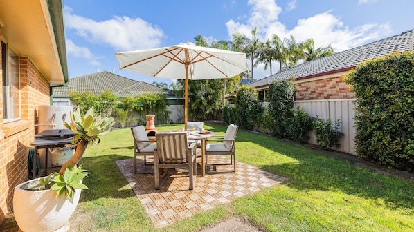 A patio with a table and chairs, a grill, and a potted plant.
