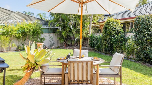 Un patio al aire libre con una mesa, sillas, un paraguas grande y una planta en maceta.
