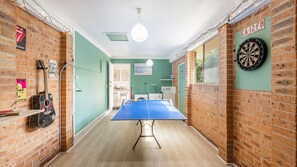 Una habitación con mesa de ping pong, dardos y una guitarra frente a una pared de ladrillo.