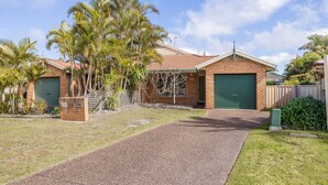 A residential property with a paved driveway, a brick house, and a green garage door. - Pet friendly Driftwood Cottage, 1-28 Farm Rd - W-Fi, Air Con and ground floor (Fingal Bay)