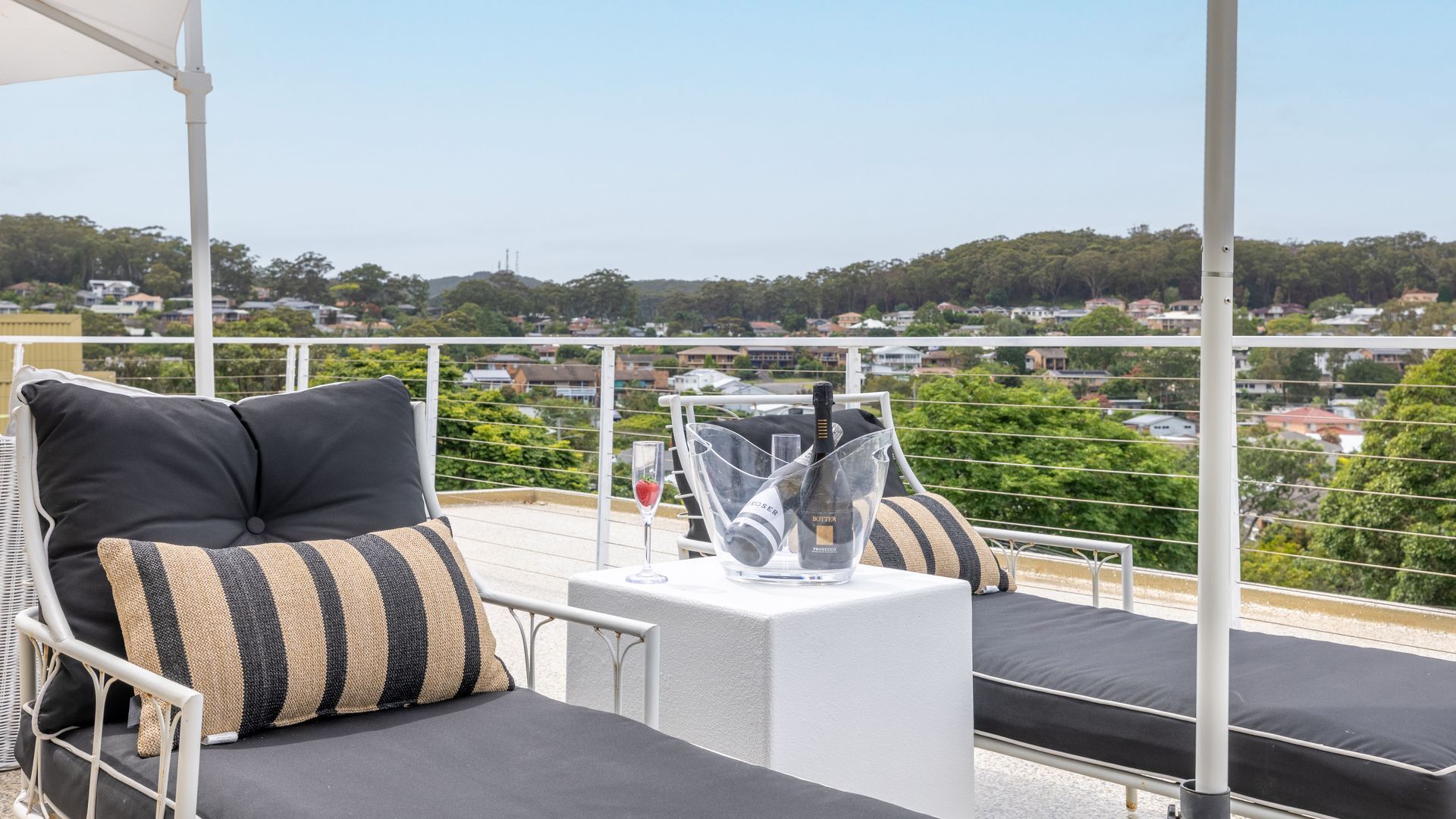 A balcony with two lounge chairs, a table with a bottle of wine, and a clear glass.