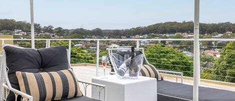 A balcony with two lounge chairs, a table with a bottle of wine, and a clear glass.