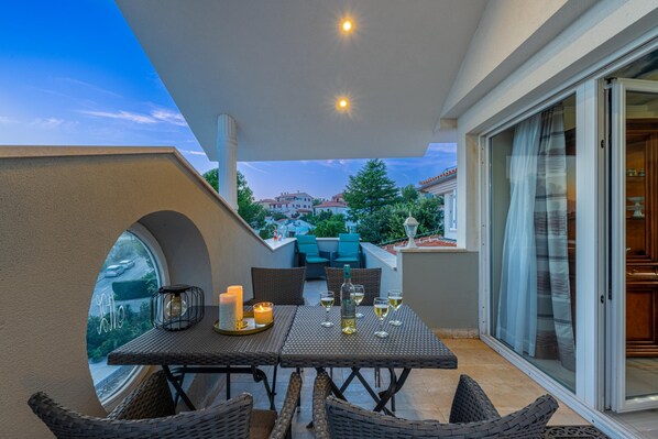 A balcony with a table set for dining, wicker chairs, and a view of the cityscape.