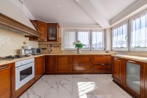 A modern kitchen with wooden cabinets, a built-in oven, a microwave, and a large window with curtains.