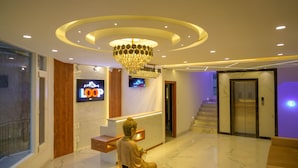 Un hall d’entrée moderne avec un sol en marbre, un comptoir d’accueil, une statue de Bouddha, un lustre et un écran de télévision.