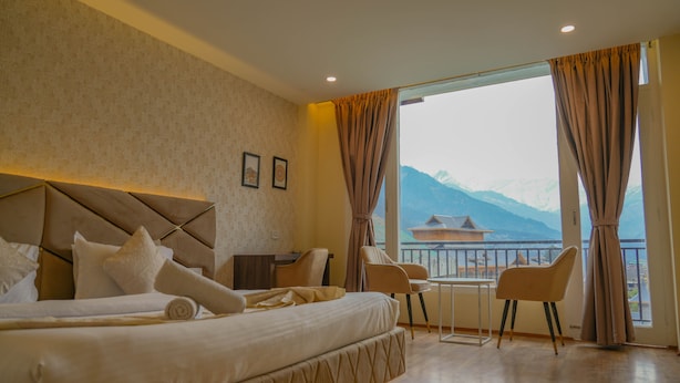 Une chambre d’hôtel avec un grand lit, un bureau et une vue sur les montagnes par la fenêtre.
