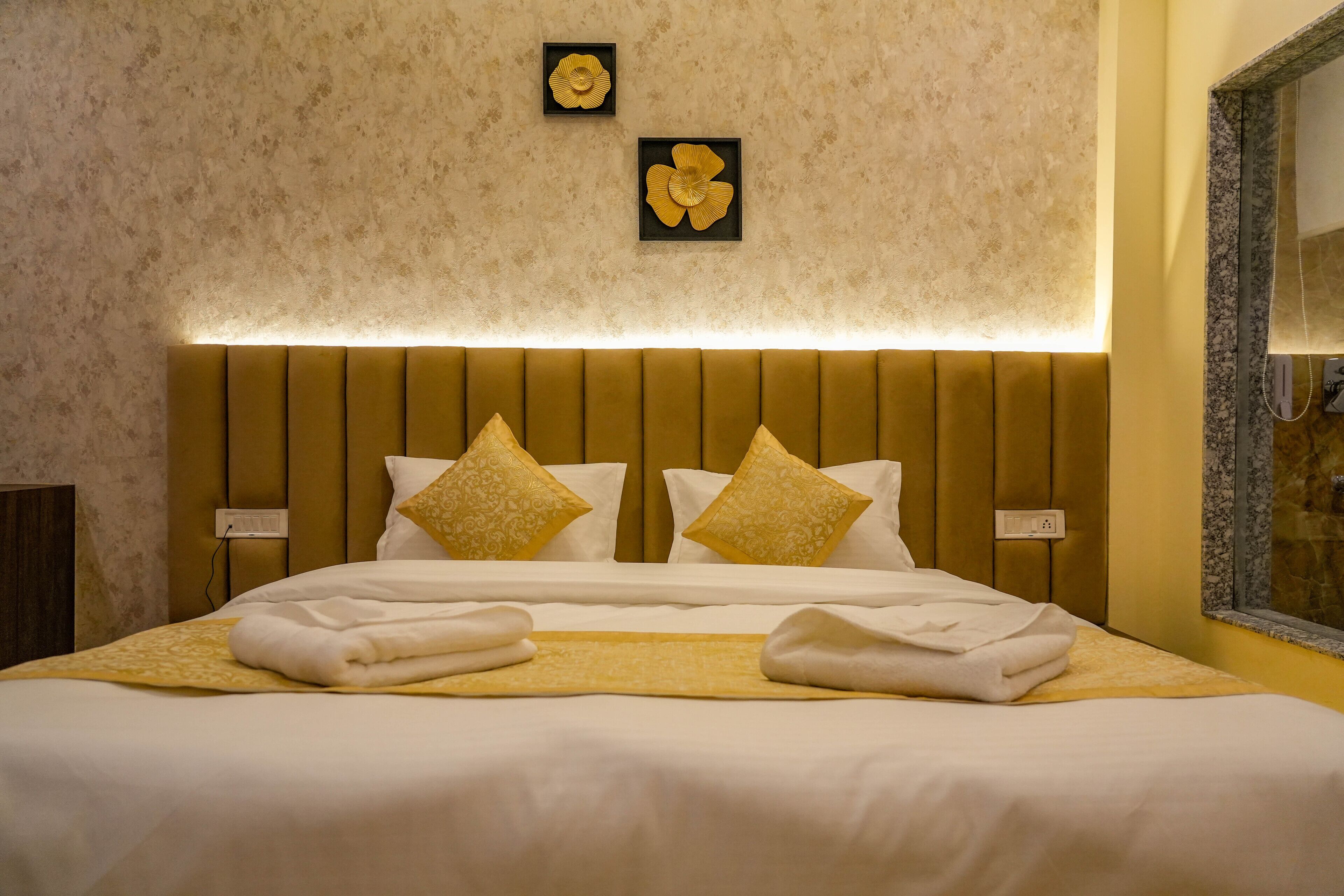 A neatly made bed with white linens and two decorative pillows, a wall-mounted light fixture, and a framed mirror.