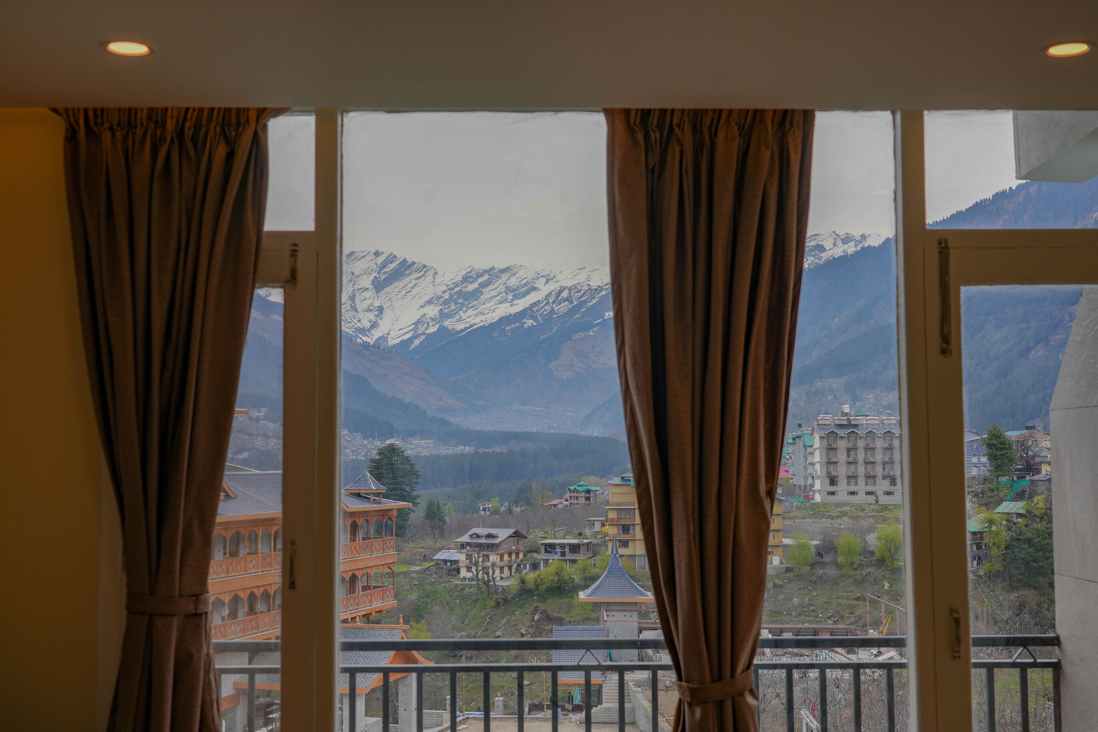A room with a large window overlooking a mountainous landscape, featuring traditional architecture and a view of the mountains.
