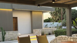 An outdoor patio with a wooden table and chairs, stone walls, and a view of greenery. - Άνετη βίλα οικογενειακού μεγέθους με υδρομασάζ! (Heraklion, Crete)