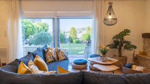 A living room with a large window, a sofa, a table, and a hanging light fixture. - Άνετη βίλα οικογενειακού μεγέθους με υδρομασάζ! (Heraklion, Crete)