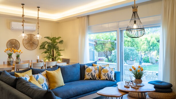 A modern living room with a blue sofa, a round coffee table, and a dining area with a white table and chairs. - Άνετη βίλα οικογενειακού μεγέθους με υδρομασάζ! (Heraklion, Crete)