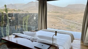 A bedroom with a bed, a laptop, and a view of a mountainous landscape. - Wake up to nature in this modern glass house (fuerteventura)