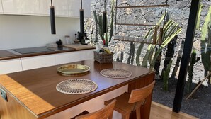 A wooden dining table with two chairs, a coffee machine, and a cactus plant in the background. - Wake up to nature in this modern glass house (fuerteventura)