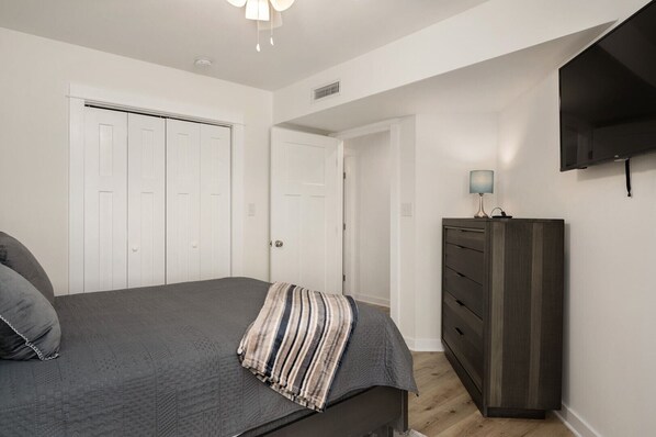 A bedroom with a bed, a dresser, a TV, and a door.