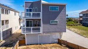 A multi-story beach house with a balcony, a second-floor window, and a view of the beach.