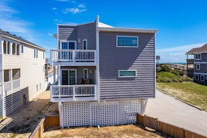 Una casa sulla spiaggia su più piani, con un balcone, una finestra al secondo piano e vista sulla spiaggia.