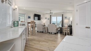 A modern kitchen with a wooden island, a dining area with striped chairs, a television, and a view of the sea.