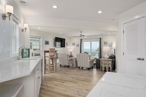 A modern kitchen with a wooden island, a dining area with striped chairs, a television, and a view of the sea.