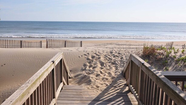 A wooden boardwalk leading to a sandy beach with the ocean in the background.