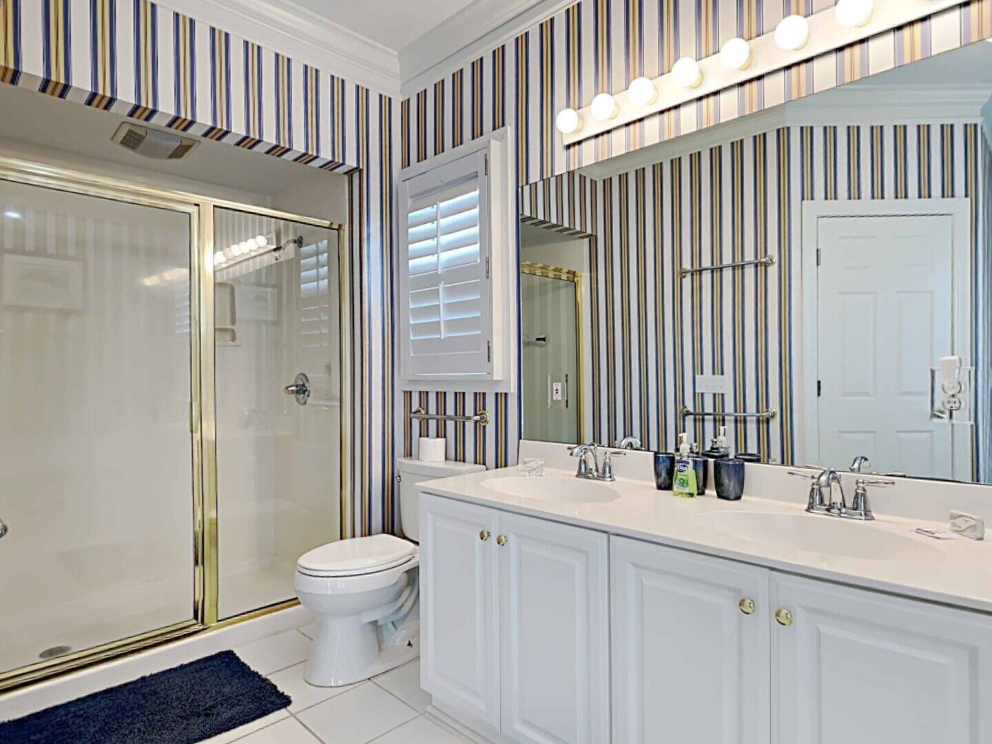 A bathroom with a walk-in shower, a toilet, a vanity with a large mirror, and striped wallpaper.
