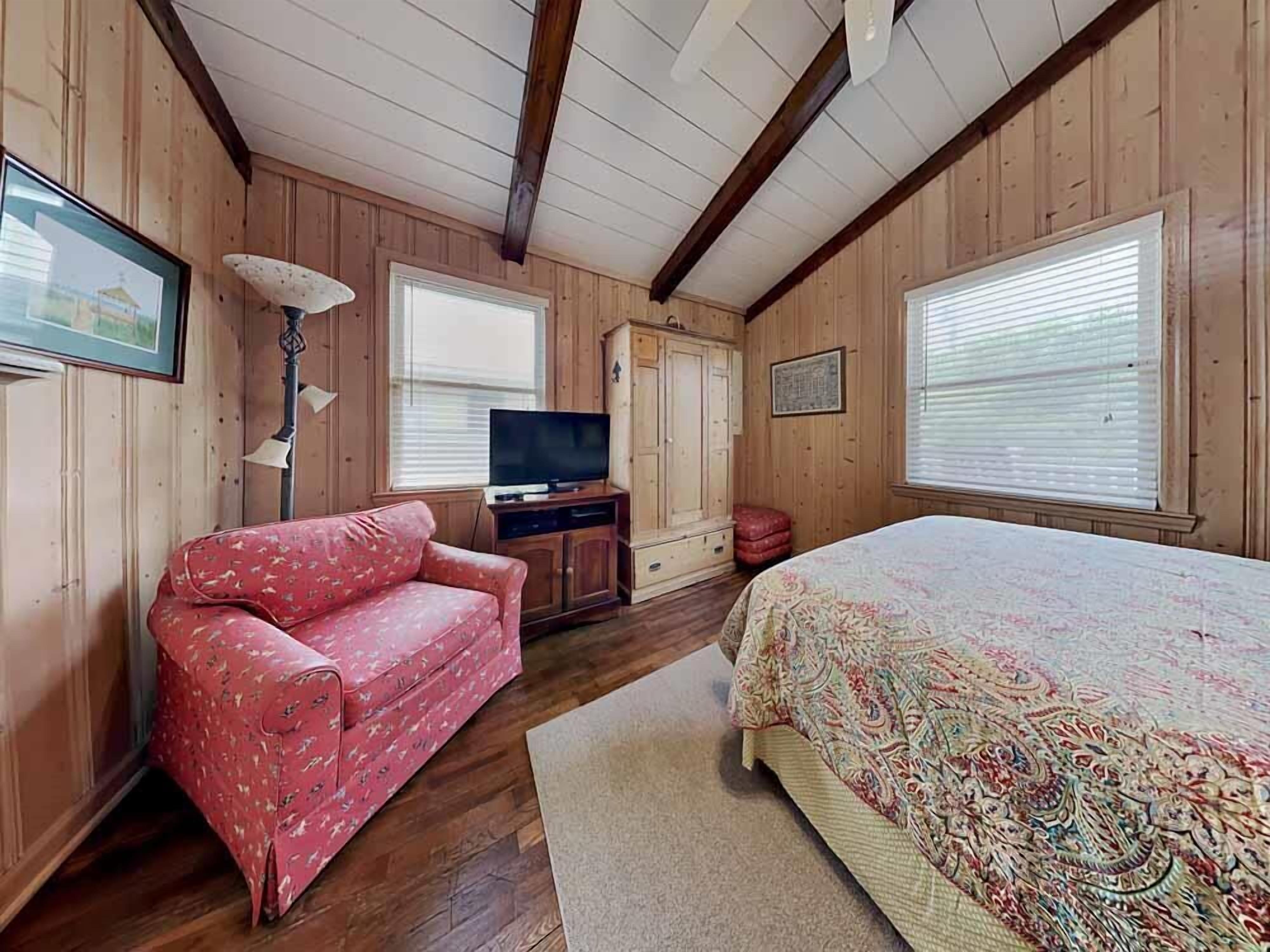 Ein Zimmer mit Holzvertäfelung, einem Bett, einem roten, gemusterten Sofa, einem Fernseher und einem Schrank.