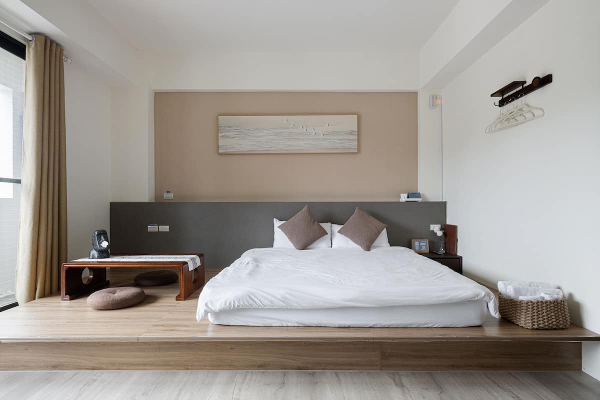 Una habitación de hotel moderna con una cama grande, una mesita de noche, un escritorio pequeño y un zapatero adherido a la pared.