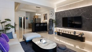 A modern living room with a sofa, ottoman, and coffee table. There is a kitchen area with a refrigerator and a dining space with bar stools. - YUJING NU TIME (Tainan)