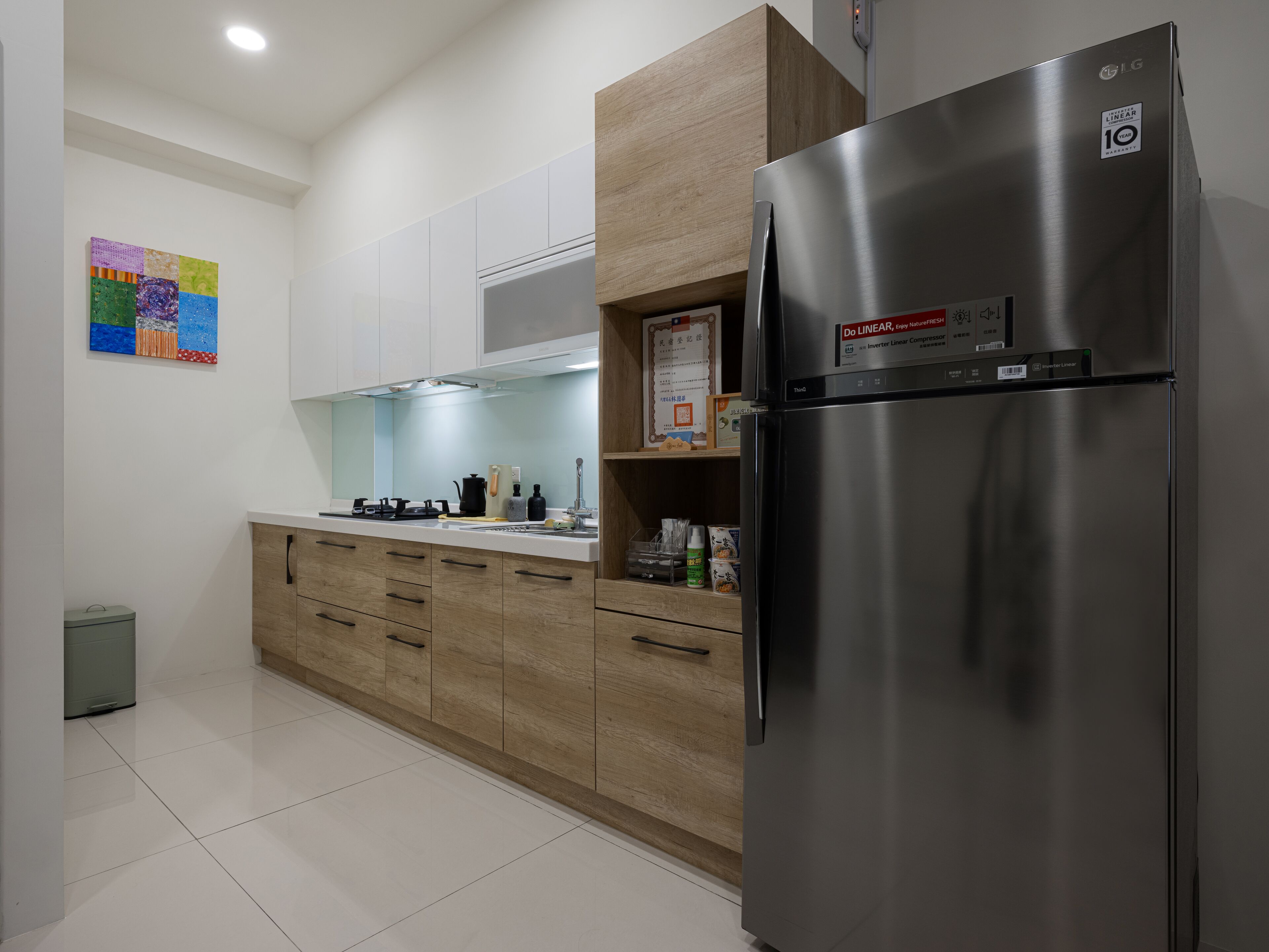 A modern kitchen with a stainless steel refrigerator, wooden cabinets, and a tiled floor.