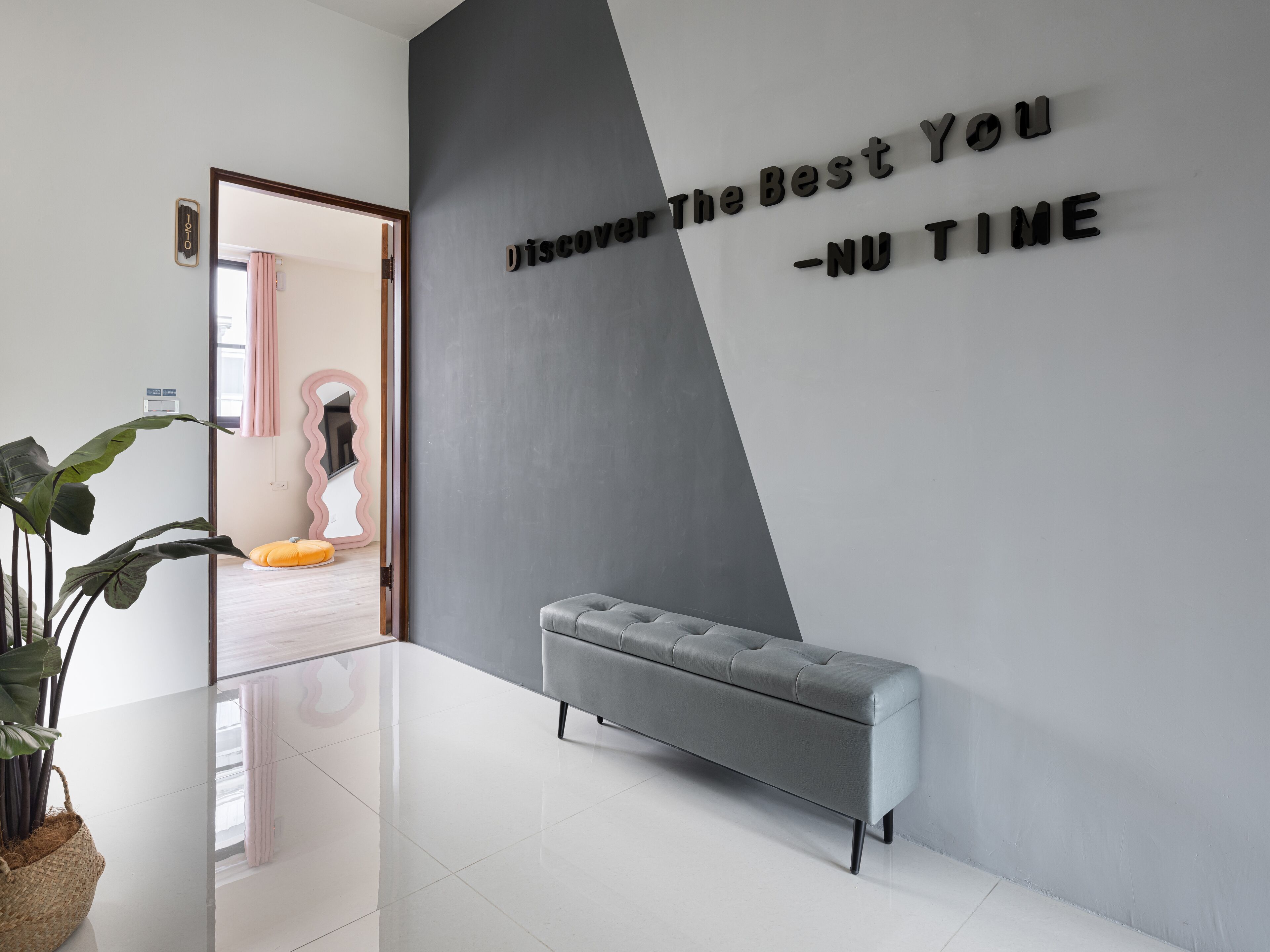 Eine moderne Lobby mit grau-weißer Farbgestaltung, einer Bank und einem motivierenden Zitat an der Wand.