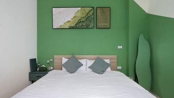 Un dormitorio con pared verde, cabecera de madera, cubrecama blanco y dos almohadas. Hay dos cuadros enmarcados en la pared.