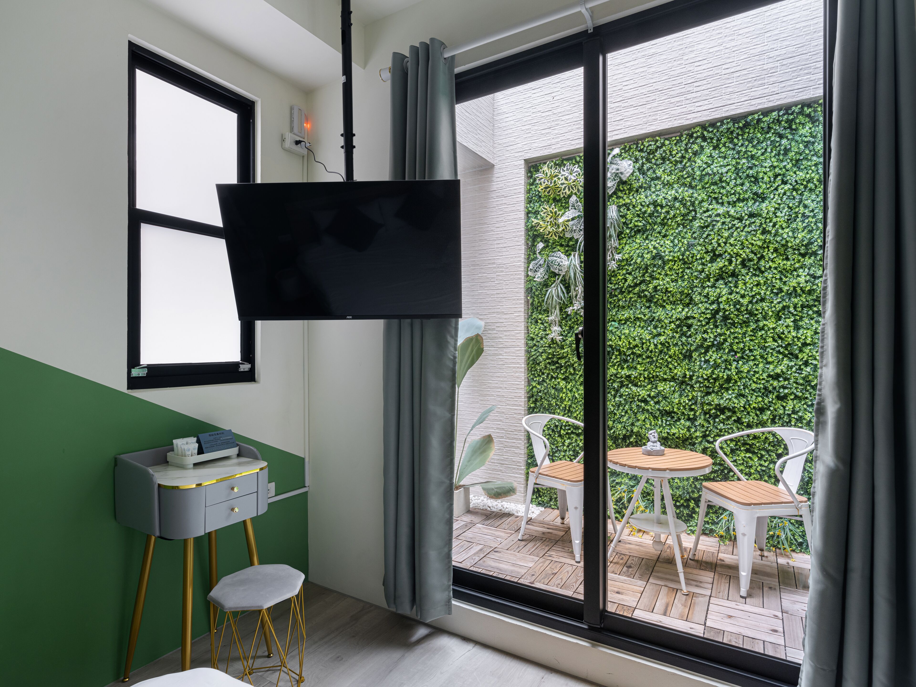 A modern room with a flat-screen TV mounted on the wall, a small desk with a chair, and a view of an outdoor patio with a table and chairs.