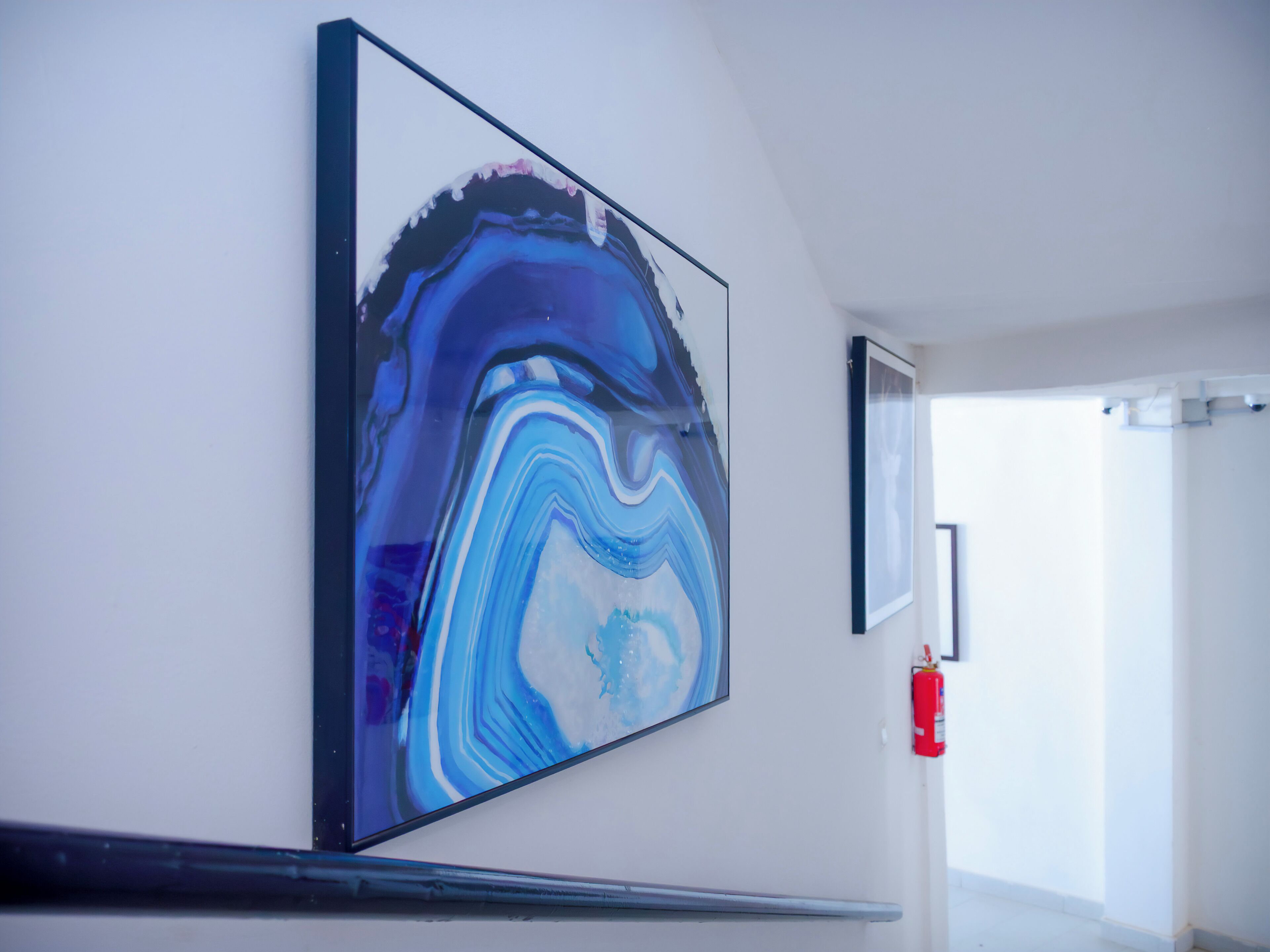 A hallway with a large abstract painting on the wall, a fire extinguisher, and a door leading to another room.